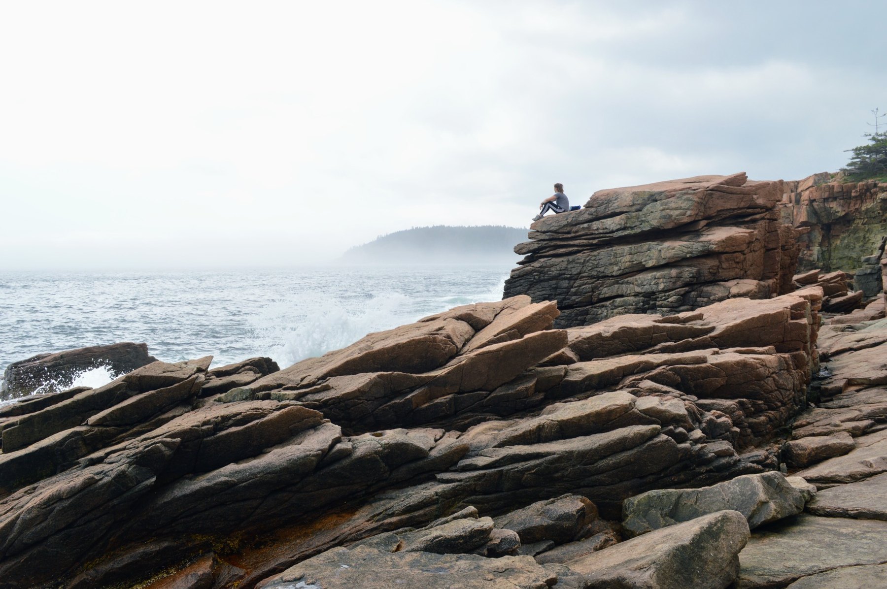 A person sitting on coastal rocks above open water