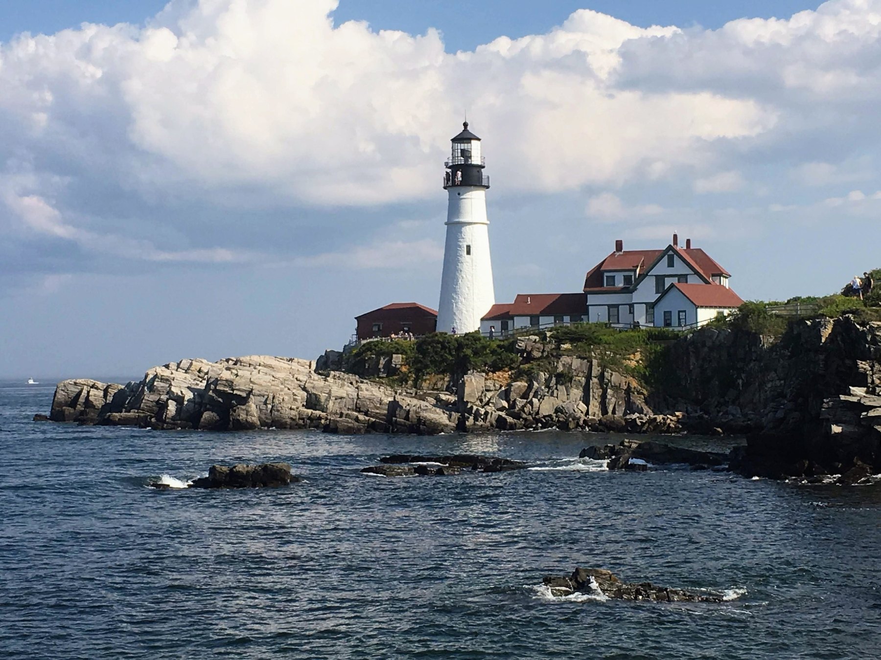 White lighthouse on a rocky coastline beneath large clouds