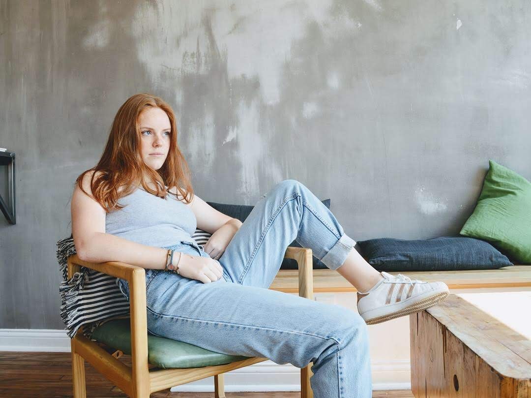 Red-haired portrait seated in a chair against a gray wall